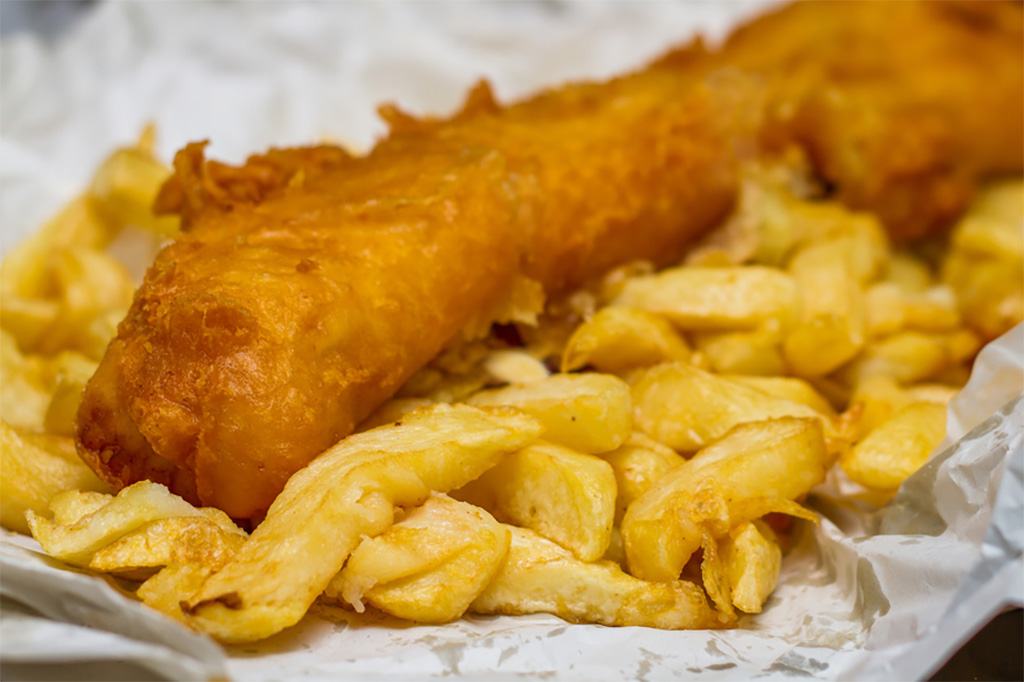 Fried battered fish served on a bed of golden chips, displayed on white paper